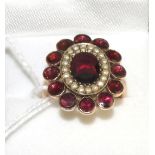 A garnet and seed pearl cluster ring, an oval cut garnet in a yellow claw setting within a border of