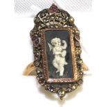 A garnet and marcasite set mourning ring, with a central painted panel depicting a putti with a