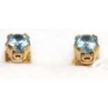 A pair of aquamarine stud earrings, a round cut aquamarine in a yellow claw setting and above a