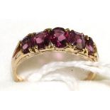 A garnet ring, five graduated vari-cut garnets in yellow claw settings, to tapering shoulders on a