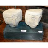 Two carved stone heads on polished slate base