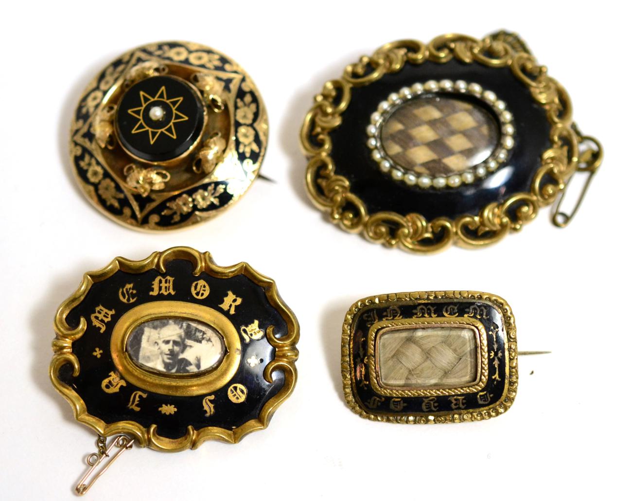 A group of four Victorian enamel and yellow metal mounted mourning brooches