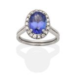 A Tanzanite and Diamond Cluster Ring, an oval cut tanzanite in a claw setting, within a border of