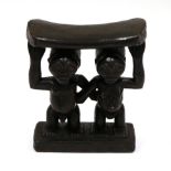 A Luba Wood Headrest, the curved pillow resting on the heads of a man and woman standing side by