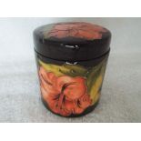 Moorcroft Pottery - a lidded cylindrical pot decorated with pink coral hibiscus on a green ground,