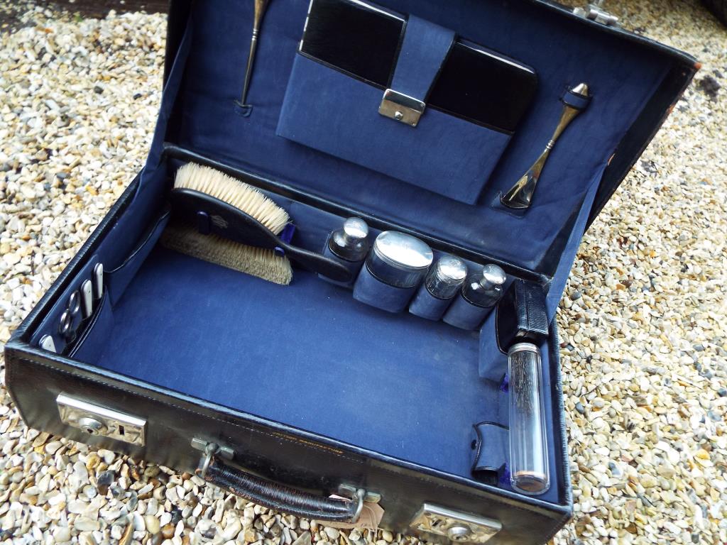 A black case with fitted interior containing a 15-piece vanity set with hallmarked silver mounts,