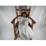 A good quality wood and wicker child's rocking chair with a child's doll with bisque head,