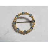 A lady's yellow metal circular brooch stamped 15 and set with seed pearls and blue zircons,