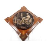 A square wooden panel with round copper plaque attached depicting a lady painting with the words