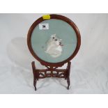 A Chinese fruitwood circular frame on stand housing a silk picture of a cat.