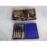 A box of unsorted costume jewellery and a cased set of six butter knives