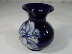 Moorcroft Pottery - a small bulbous vase with flared rim decorated with coral hibiscus on a blue