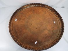 A large planished copper tray with engraved decoration, approximately 59 cm in diameter.