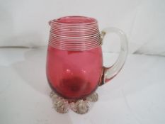 A Cranberry glass jug with white banding, approximate height 12 cm.