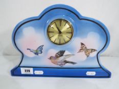 A ceramic clock decorated with butterflies and a bird.