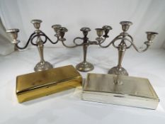 Three white metal candelabra and two large cigarette boxes.