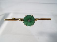 A hallmarked 18 carat gold bar brooch set with a hard stone in the form of a flower and a