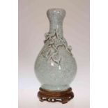 A CHINESE CELADON VASE, bottle shaped, applied with foliage, on a wooden stand.