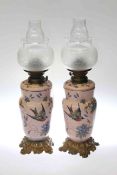 Pair of enamel and ormolu oil lamps decorated with floral and bird scenes with etched glass shades