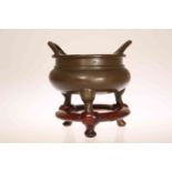 A CHINESE PATINATED BRONZE TWO-HANDLED CENSER, of squat circular form, on tripod legs,