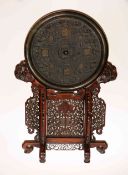 A LARGE CHINESE BRONZE MIRROR IN ARCHAIC STYLE ON A CARVED HARDWOOD STAND,