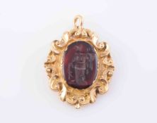 A CARNELIAN AND GILT METAL PENDANT, the carved oval carnelian depicting a standing figure,