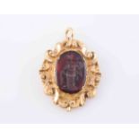 A CARNELIAN AND GILT METAL PENDANT, the carved oval carnelian depicting a standing figure,