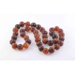 AN AMBER NECKLACE, the forty uniform carved amber beads each strung knotted into a single row.
