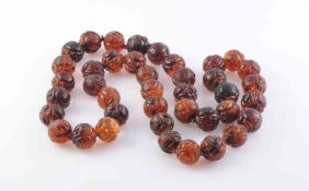 AN AMBER NECKLACE, the forty uniform carved amber beads each strung knotted into a single row.