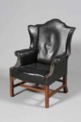 A GEORGE III STYLE LEATHER UPHOLSTERED MAHOGANY WING CHAIR, with serpentine seat rail,