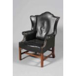 A GEORGE III STYLE LEATHER UPHOLSTERED MAHOGANY WING CHAIR, with serpentine seat rail,