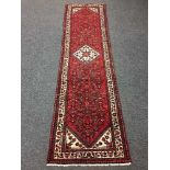 A North West Persian runner on red ground with central cream medallion, with vine borders,