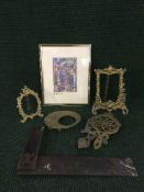 A basket of antique sets of two brass trivets, three gilt metal photograph frames,