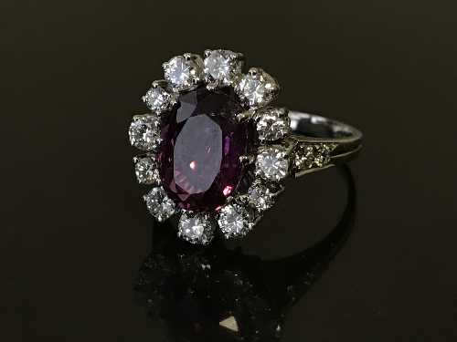 A fine ruby and diamond cluster ring, the central oval-cut ruby in a claw setting,