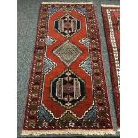 A geometric designed rug on red ground 195 cm x 91 cm
