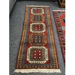 A geometric designed rug on red ground 210 cm x 80 cm