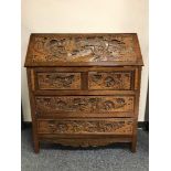 A carved oak writing bureau with oriental decoration, fitted with four drawers below, width 92 cm.