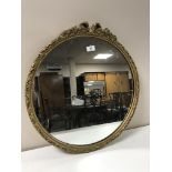 A gilt framed circular mirror with ornate bow topped frame