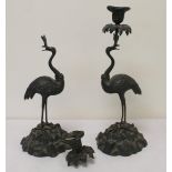 Pair of bronze candlesticks in the form of flamingos on rocky plinth bases holding foliate sconces,