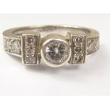 Diamond ring with collet set brilliant flanked by ten others smaller, in 9ct white gold. Size L.