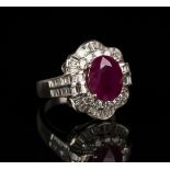 An 18ct white gold, ruby and diamond cluster ring, claw set with an oval cut ruby within a