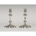 A pair of George II silver candlesticks, each urn shaped sconce on a knop stem and shaped square