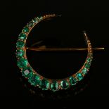 A gold and emerald brooch, designed as a crescent, mounted with a row of graduated variously cut