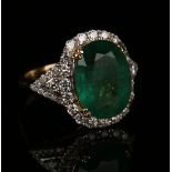 An 18ct gold, emerald and diamond ring, claw set with the oval cut emerald within a surround of