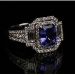 An 18ct white gold, tanzanite and diamond ring, the cushion cut tanzanite within a surround of