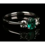 An 18ct white gold, emerald and diamond ring, claw set with the oval cut emerald between two