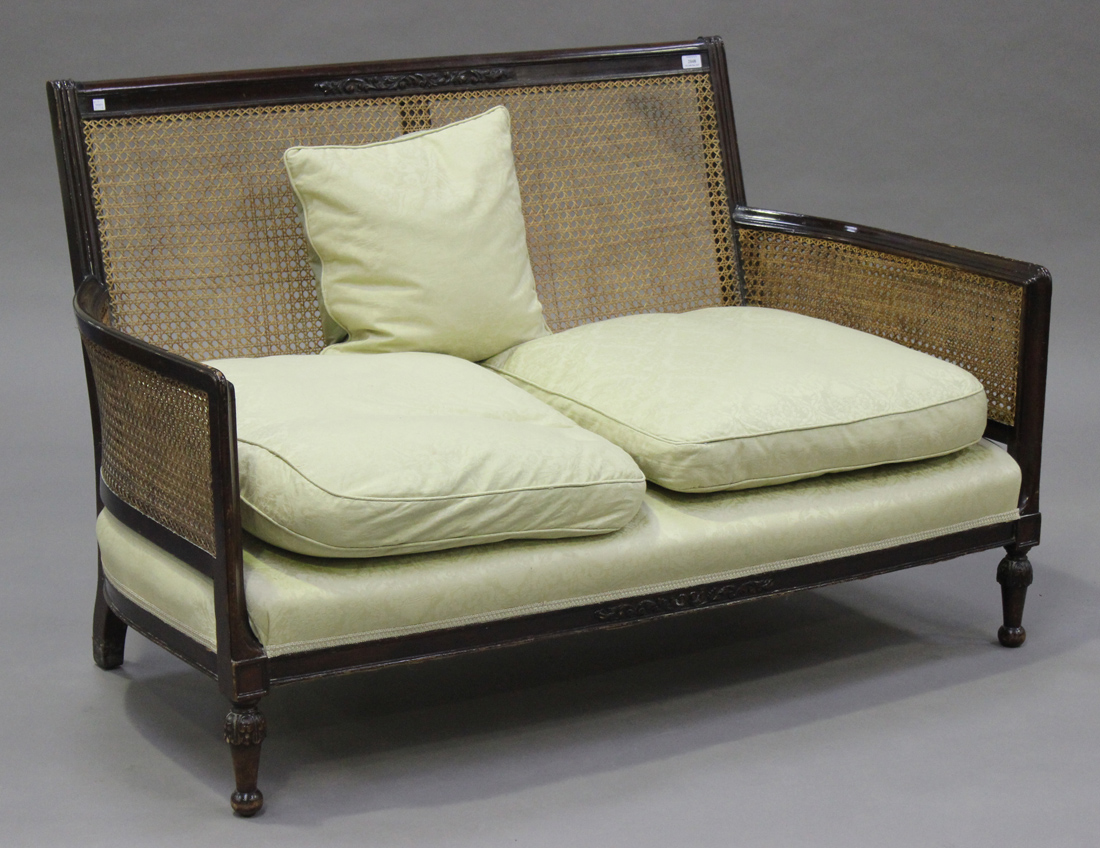 A George V mahogany framed bergère two-seat settee, the back rail carved with floral scrolls above a