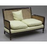 A George V mahogany framed bergère two-seat settee, the back rail carved with floral scrolls above a