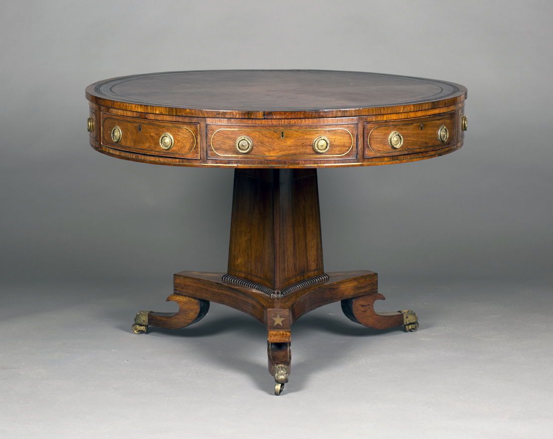 A Regency rosewood and brass inlaid drum top library table, the circular top inset with red