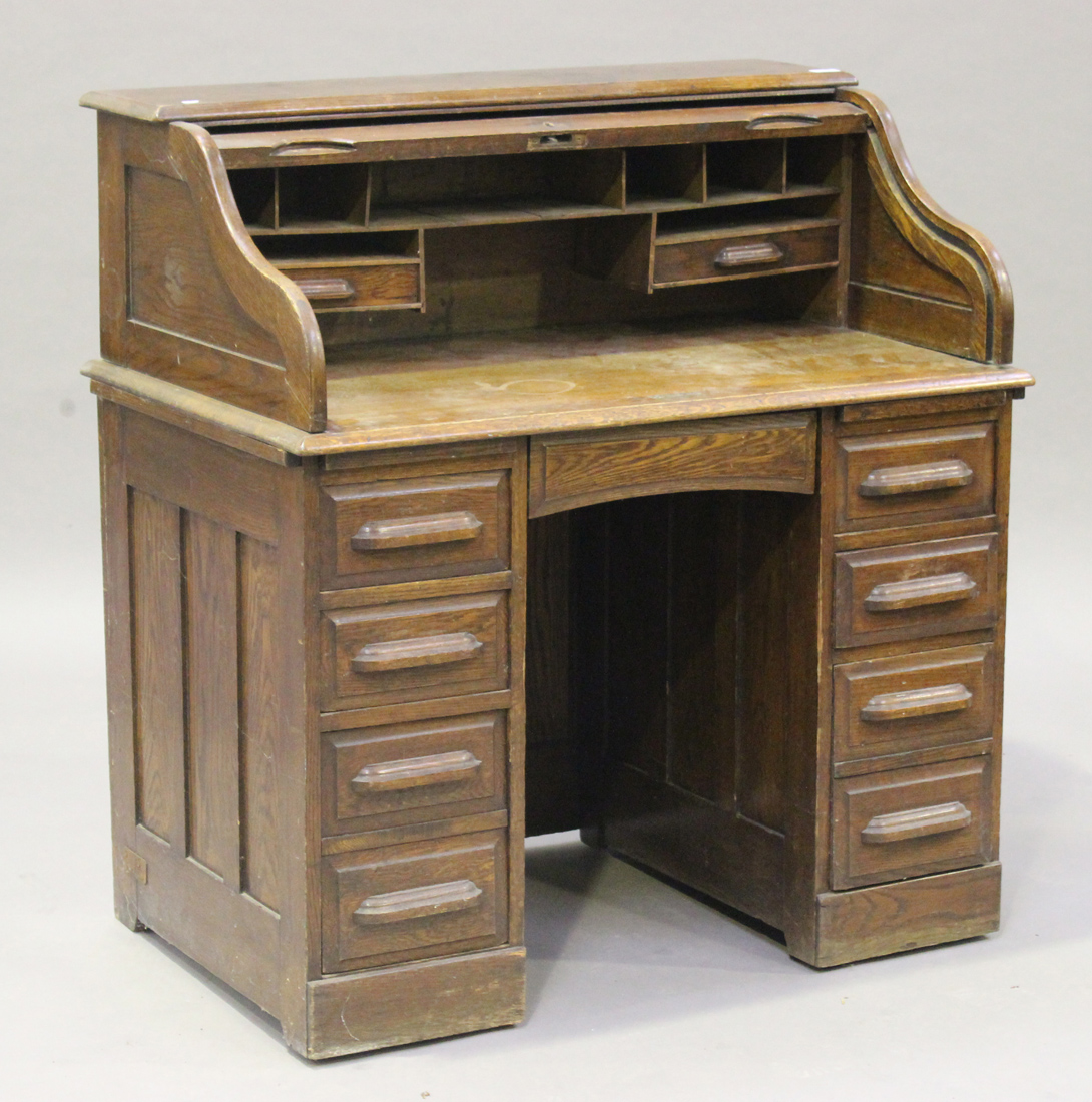 An early 20th century oak roll-top twin pedestal desk, the tambour front revealing a fitted interior